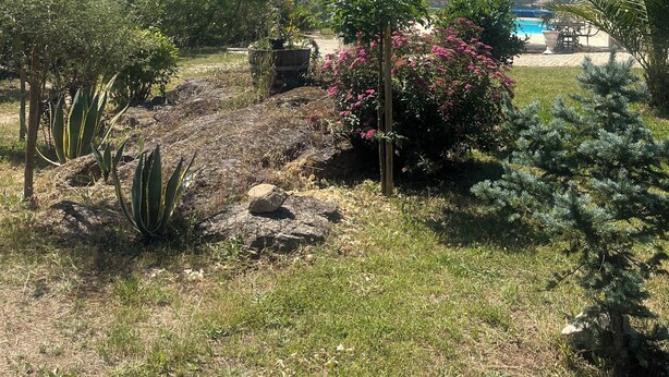 A garden with a pool, a stone building, and a view of distant mountains.