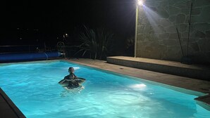 A swimming pool at night with a person in the water, surrounded by stone walls and a staircase.