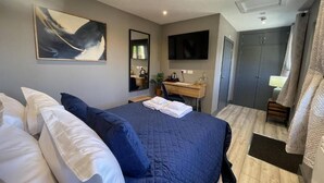 Um quarto com cama, escrivaninha, televisão e guarda-roupa.