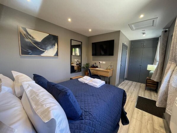 A bedroom with a bed, a desk, a TV, and a wardrobe.