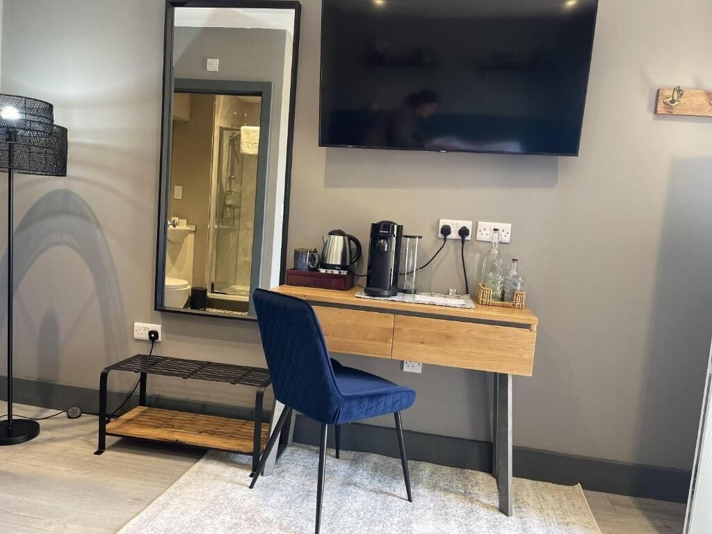 Una habitación de hotel moderna con un escritorio de madera, una silla azul, un televisor de pantalla plana, un espejo y un pequeño banco.