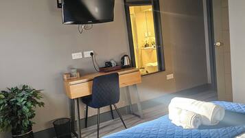 A hotel room with a bed, a desk with a chair, a television, and a mirror.