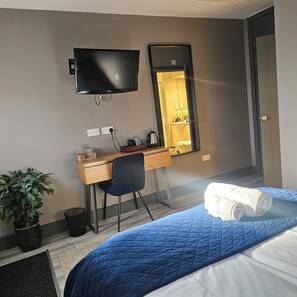A hotel room with a bed, a desk with a chair, a television, and a mirror.
