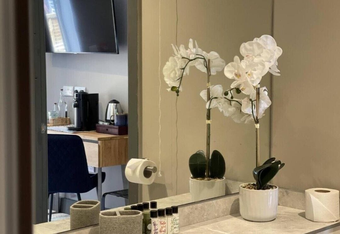 A bathroom with a mirror, white orchids, a sink, and toiletries.