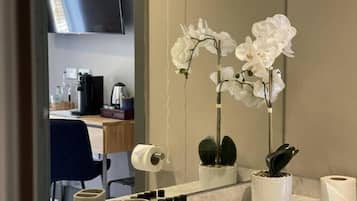Un baño con espejo, orquídeas blancas, lavamanos y artículos de aseo.
