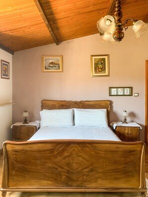 Uma cama de madeira com cabeceira, duas mesas de cabeceira com abajures e quadros nas paredes.