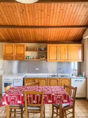 Uma cozinha com armários de madeira, fogão e mesa de jantar com cadeiras.