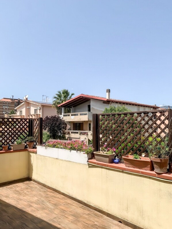 Um bairro residencial com varanda, plantas em vasos e céu claro.