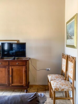 Ein Zimmer mit einem Holzkasten, einem Fernseher, einer Bank und einem Bild an der Wand.