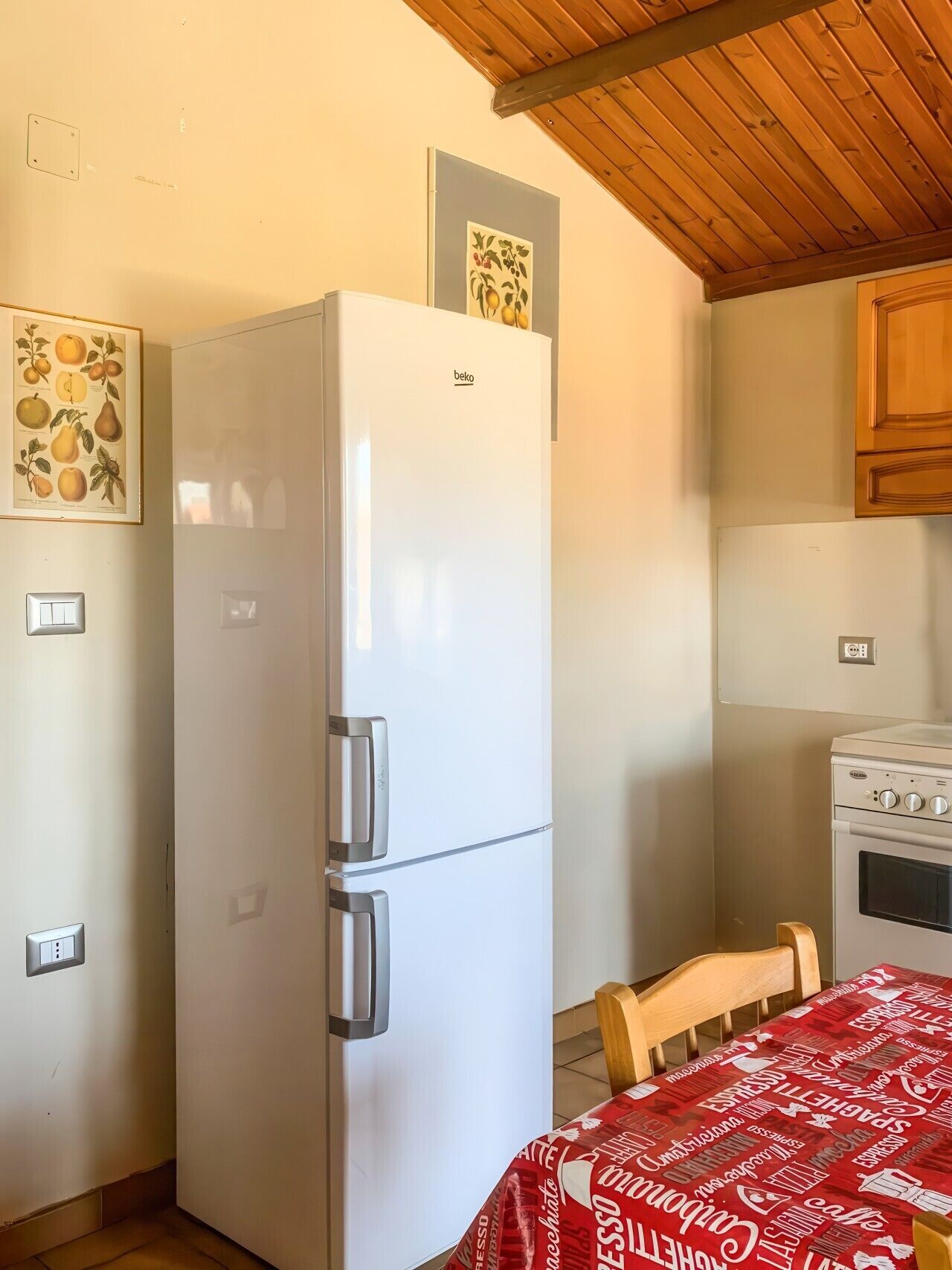 Una cocina con un refrigerador blanco, armarios de madera, una mesa con mantel rojo y un horno empotrado.