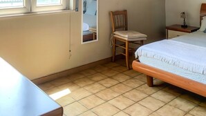 A bedroom with a wooden ceiling, a bed, a chair, a nightstand, a mirror, and a window with a view of greenery. - Casa Paola - Iglesias (Iglesias)