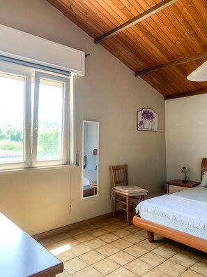 Ein Schlafzimmer mit Holzboden, einem Bett, einem Sessel, einem Nachttisch, einem Spiegel und einem Fenster mit Blick auf Grünflächen.