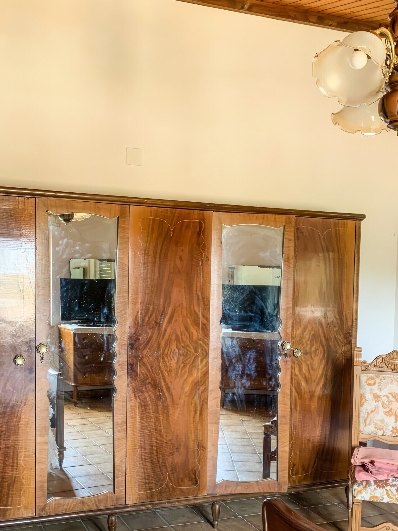 A wooden wardrobe with mirrored doors, a ceiling light fixture, and a tiled floor.