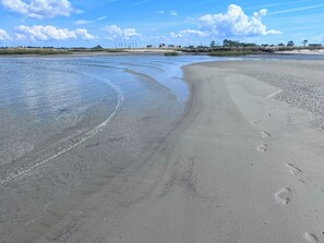 A beach with clear water, footprints, and a distant shoreline with buildings. - Water Front 1 bedroom house on tranquil Smith Island (Smith Island)