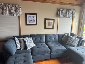 A sectional sofa with patterned cushions, framed artwork on the wall, and window treatments with a tree pattern.