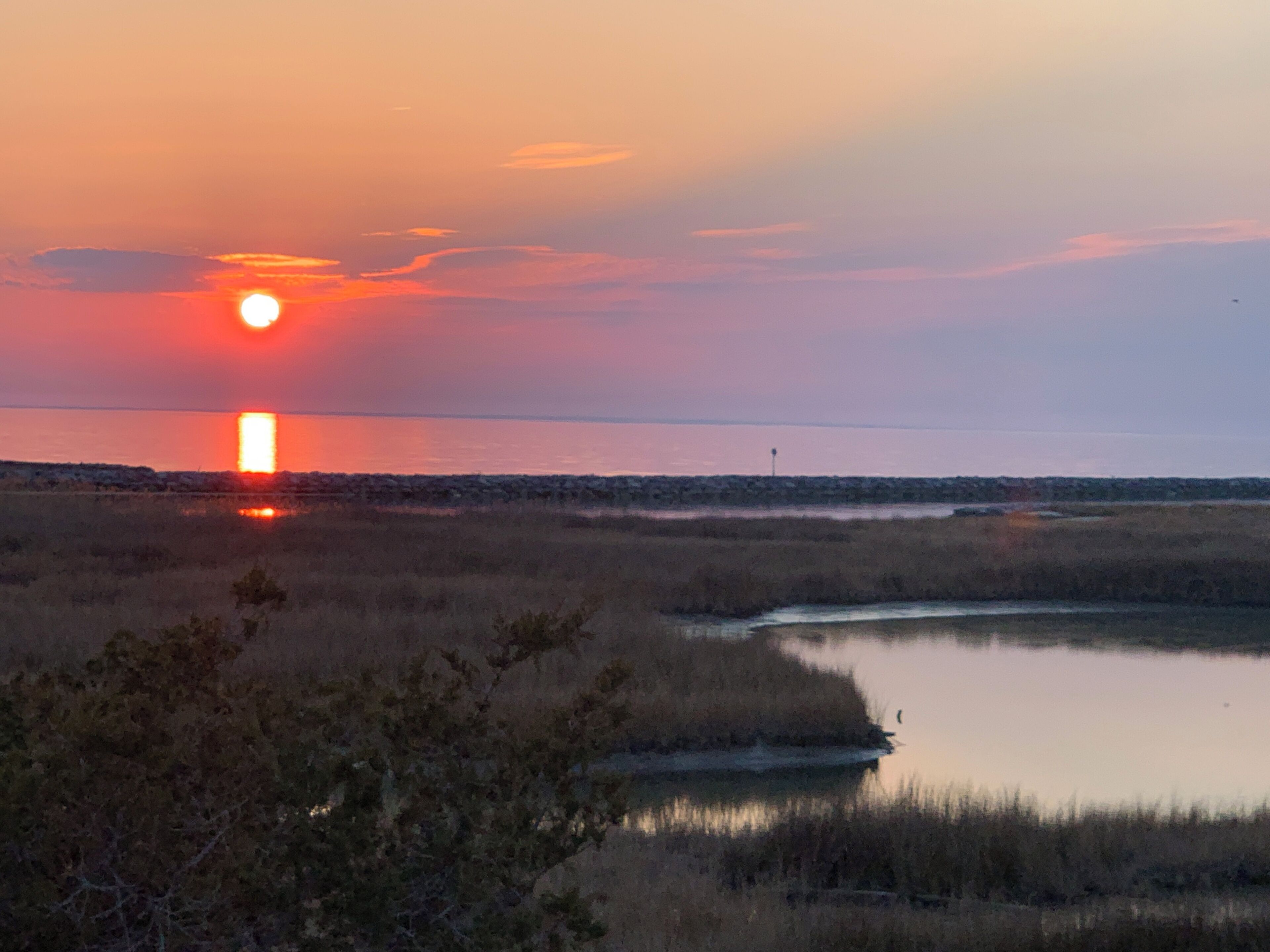 A sunset over a flat landscape with a body of water and sparse vegetation.