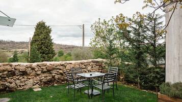 Un muro de piedra, un patio cubierto de césped y una mesa con sillas.