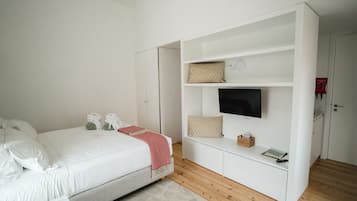 Un dormitorio con una cama, un televisor sobre un estante blanco y una puerta con un letrero rojo.