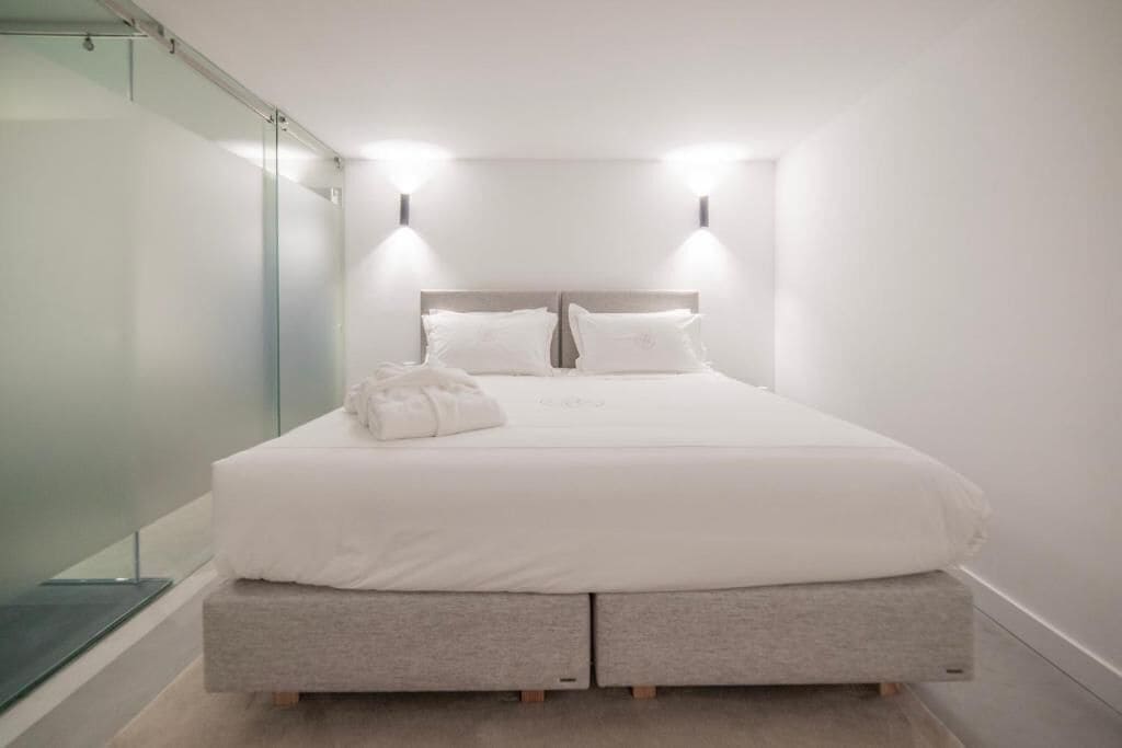A modern bedroom with a bed, bedside lamps, and a glass partition.