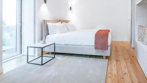 Un dormitorio con cama, mesita de noche, ventana y vistas al exterior.