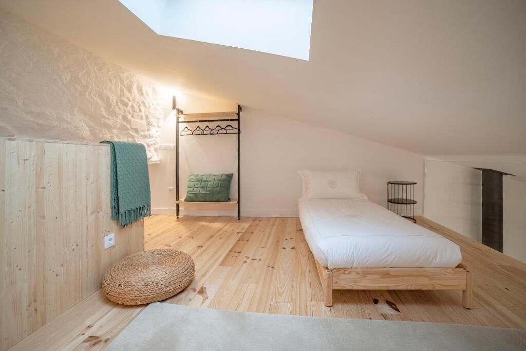 Une chambre avec un plafond en pente, un lit superposé, un pouf rond en osier et une petite table de chevet.