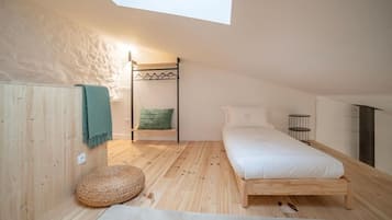 Une chambre avec un plafond en pente, un lit superposé, un pouf rond en osier et une petite table de chevet.