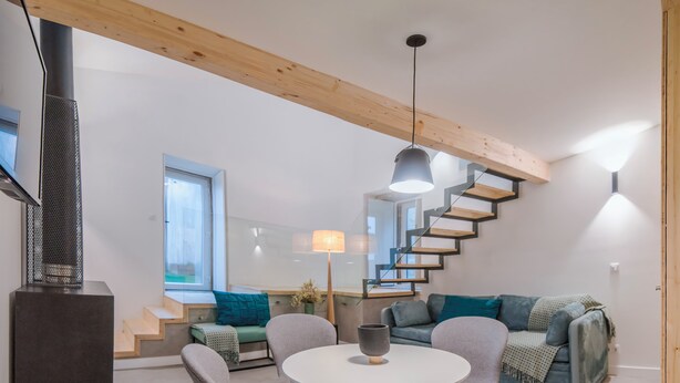 Un espacio de estar moderno con una mesa redonda, cuatro sillas grises, un sofá, una escalera y un televisor montado en la pared.