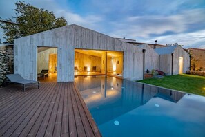 A modern house with a swimming pool, wooden deck, and a stone wall.