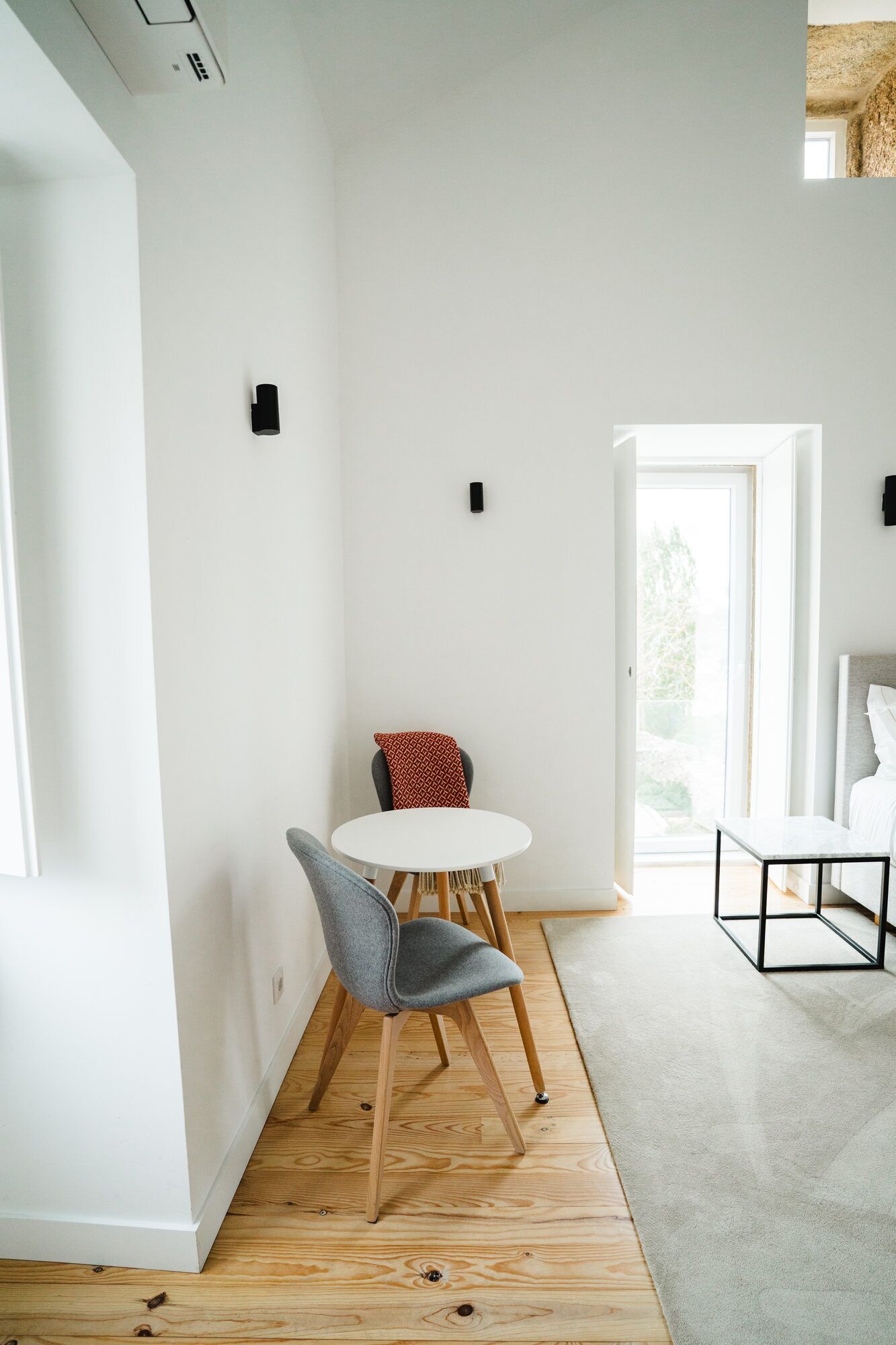 A modern interior with a round table, a grey chair, and a bed with a white headboard.