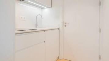 A small, compact kitchen with white cabinetry, a single faucet, and a wooden floor.