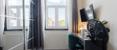 Une pièce comprenant un bureau, une chaise, un téléviseur, un radiateur et une fenêtre avec des rideaux.