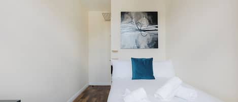 A hotel room with a bed, white linens, a blue pillow, and a painting on the wall.