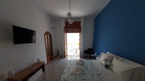 A bedroom with a bed, a bench, a TV, and a view of the outside. - Sicilia Charme - Design and the Sea in Avola (Avola)