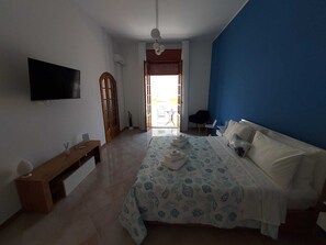 Ein Schlafzimmer mit Bett, einer Sitzbank, einem Fernseher und Blick ins Freie.