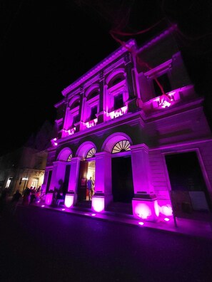 Ein Gebäude mit Rundbogenfenstern und einem zentralen Eingang, beleuchtet durch violette Lichter.