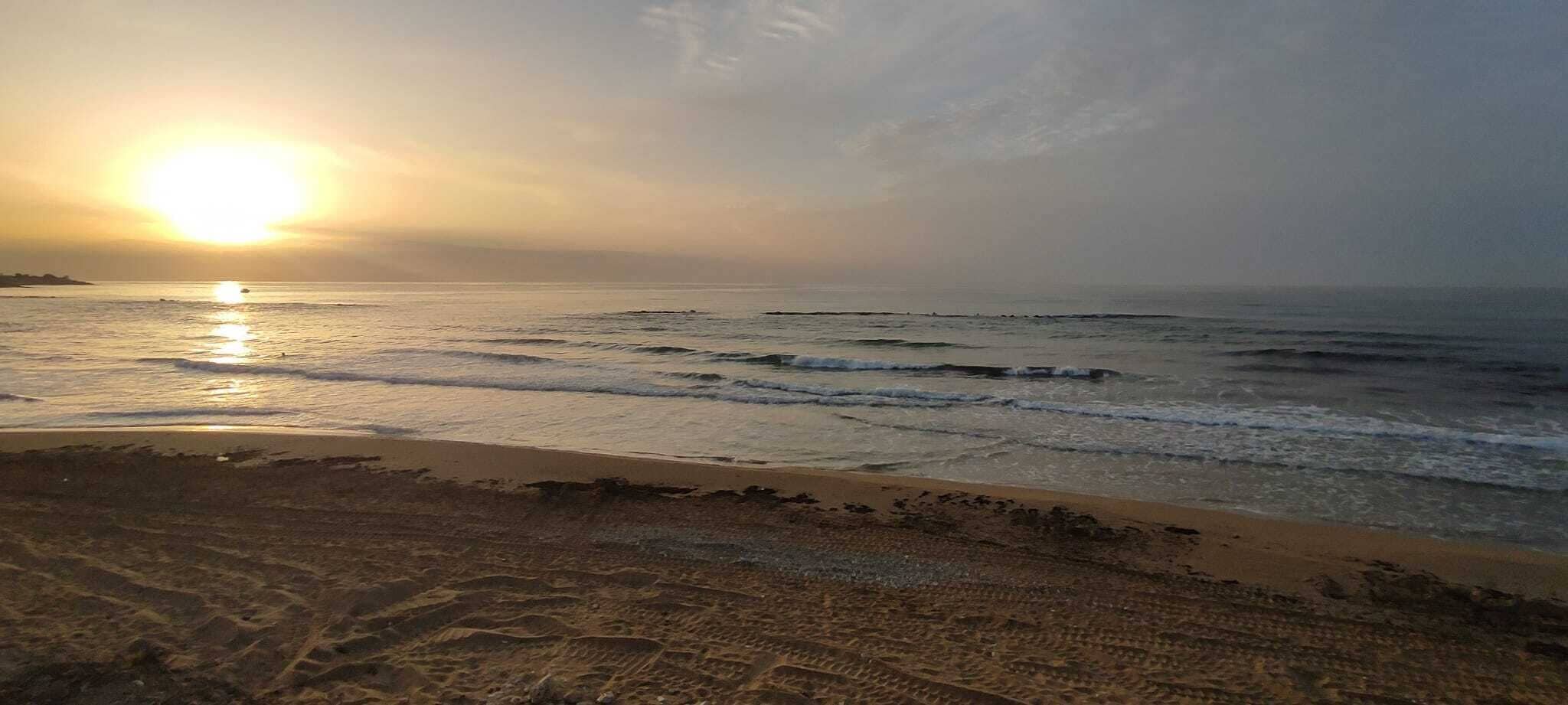 Ein Strand mit untergehender Sonne über dem Ozean, der eine ruhige Atmosphäre schafft.
