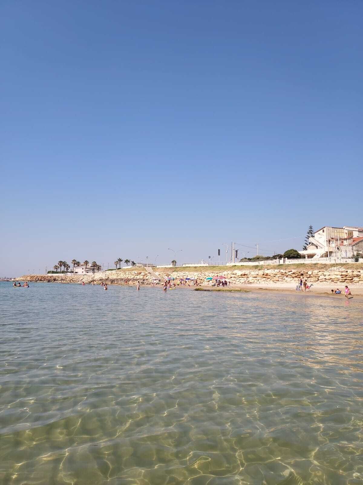 A beach with clear water, people swimming, and buildings in the background.