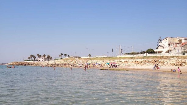 A beach with clear water, people swimming, and buildings in the background. - Sicilia Charme - Design and the Sea in Avola (Avola)