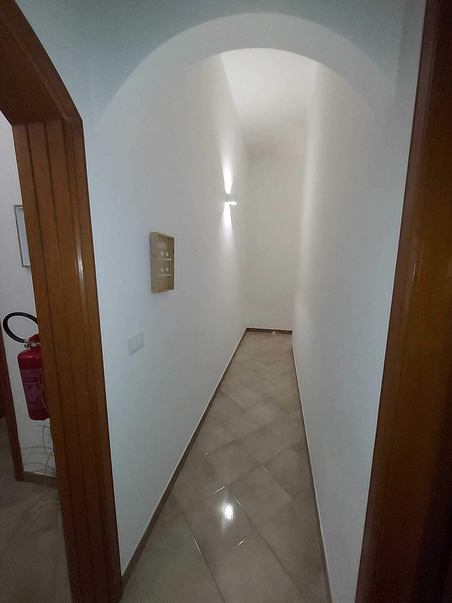 A hallway with a tiled floor, a fire extinguisher, and a wall-mounted emergency call station.