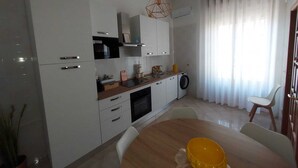 A modern kitchen with white cabinets, a wooden countertop, and a dining area with a round table. - Sicilia Charme - Design and the Sea in Avola (Avola)