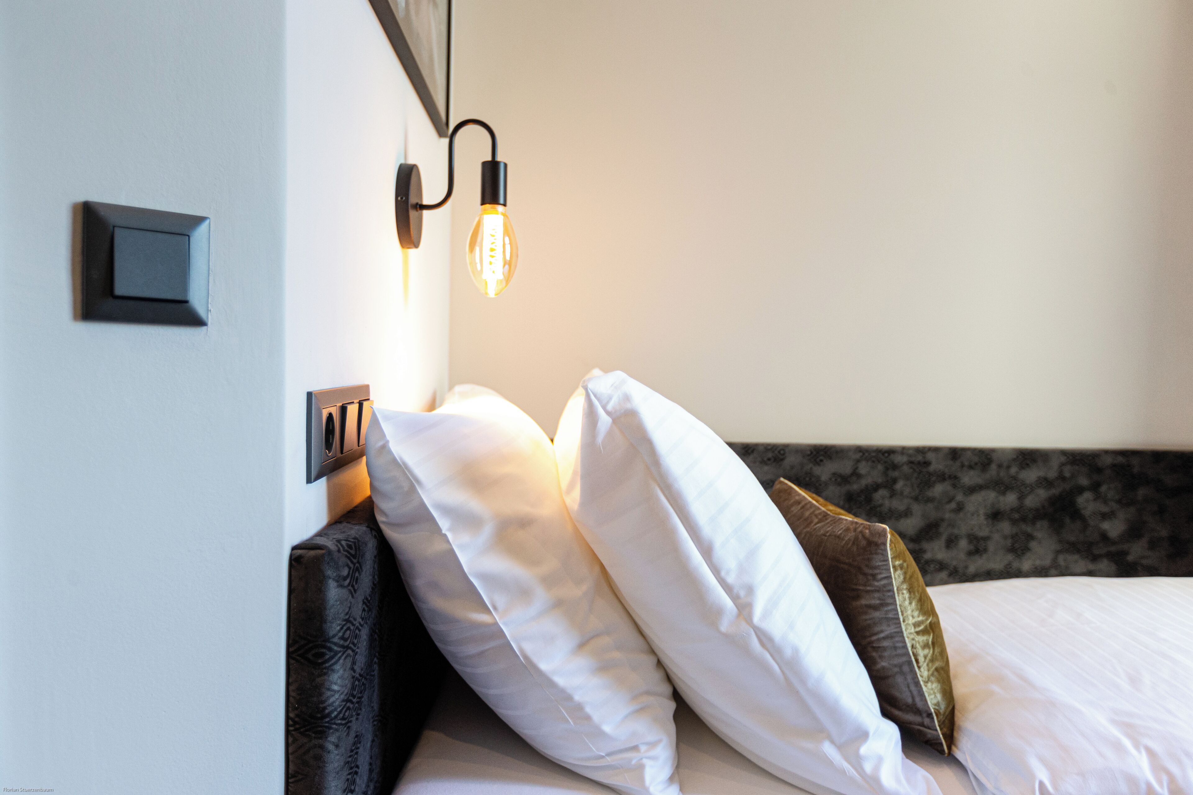 A neatly made bed with white and brown pillows, a dark headboard, and a wall-mounted light fixture.