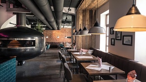 A restaurant interior with a brick wall, wooden ceiling, and a large grill. Tables and chairs are arranged for dining. - Boutique Hotel Kolbeck (Vienna)