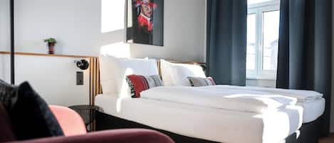 Una habitación de hotel moderna con una cama grande, una mesita de noche, una planta pequeña en maceta y una ventana con cortinas.