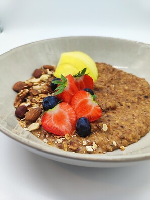 Uma tigela de mingau coberto com morangos, mirtilos, amêndoas e uma fatia de limão.