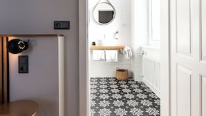 A bathroom with a black and white patterned floor, a wooden vanity, a mirror, and a radiator. - Boutique Hotel Kolbeck (Vienna)