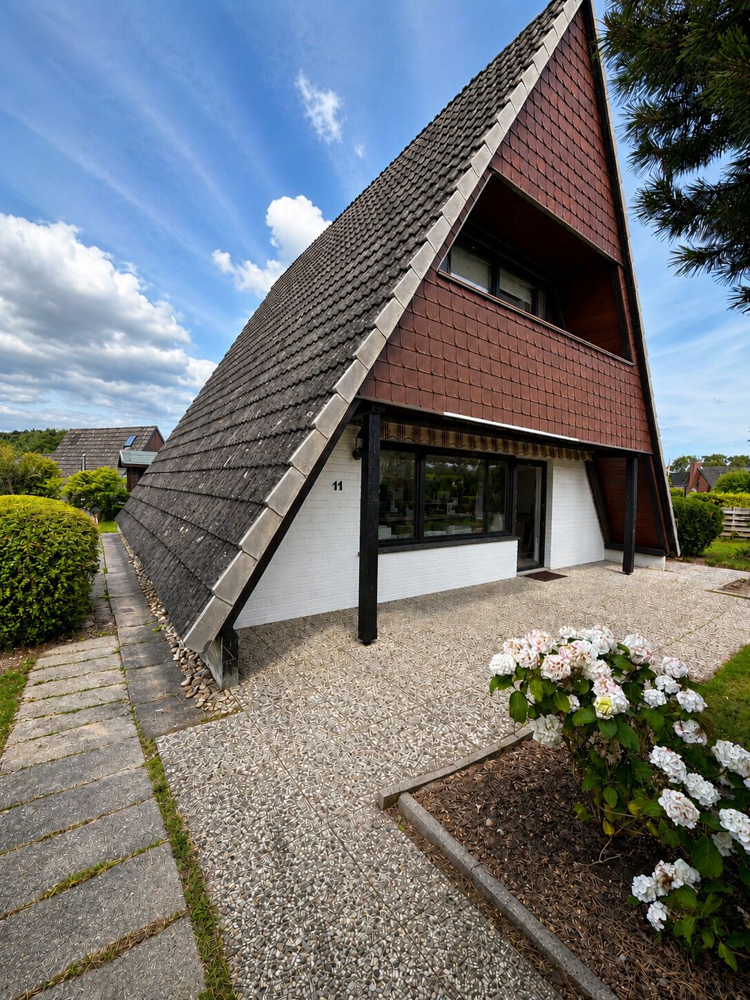 A modern house with a sloped roof, a visible number '11' on the side, and a gravel driveway.