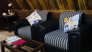 Ein gemütliches Zimmer mit schrägen Wänden, einer schwarzen Ledersofa mit gestreiften Kissen, einem kleinen Holztisch und einem Beistelltisch mit einer Lampe.