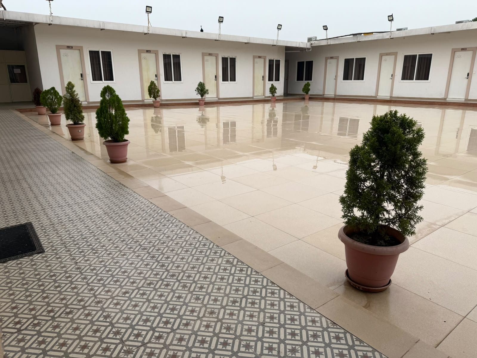 A clean, tiled courtyard with potted plants and a row of doors.