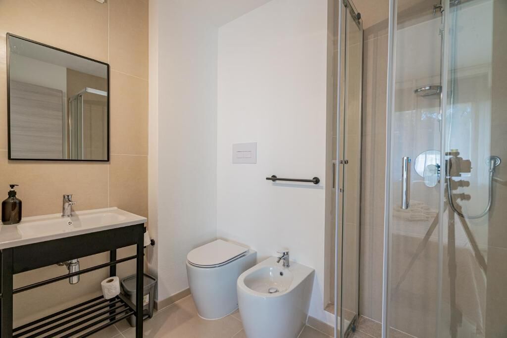 A modern bathroom with a glass shower enclosure, a white sink, a bidet, and a toilet.