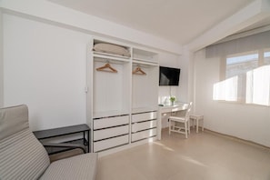 Una habitación con cama, escritorio y silla, armario con espacio para colgar y televisor en la pared.